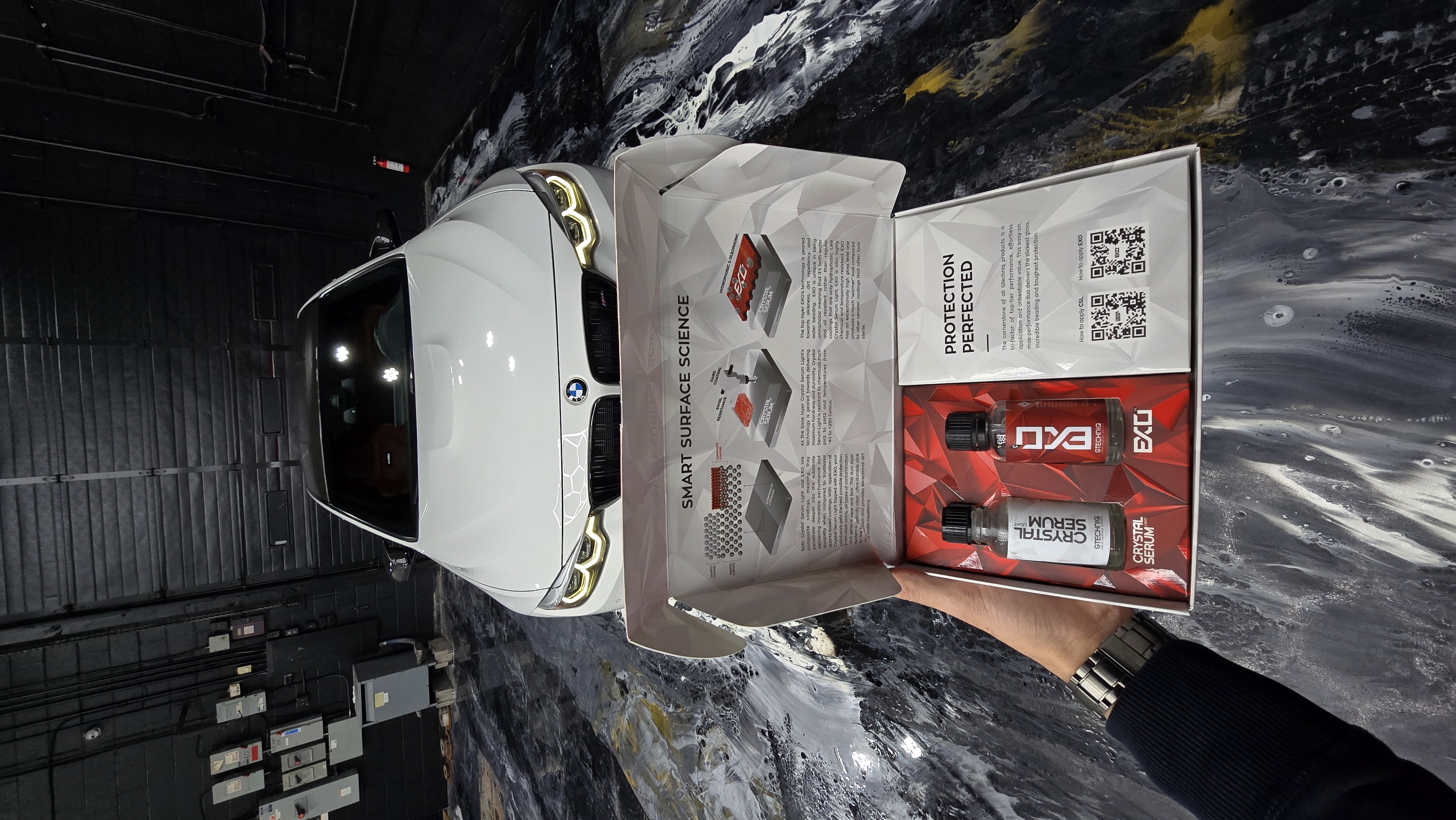 Crystal Serum Light + EXO v5 product box held in front of a white BMW M4 inside Jester Werks Mississauga ceramic coating studio
