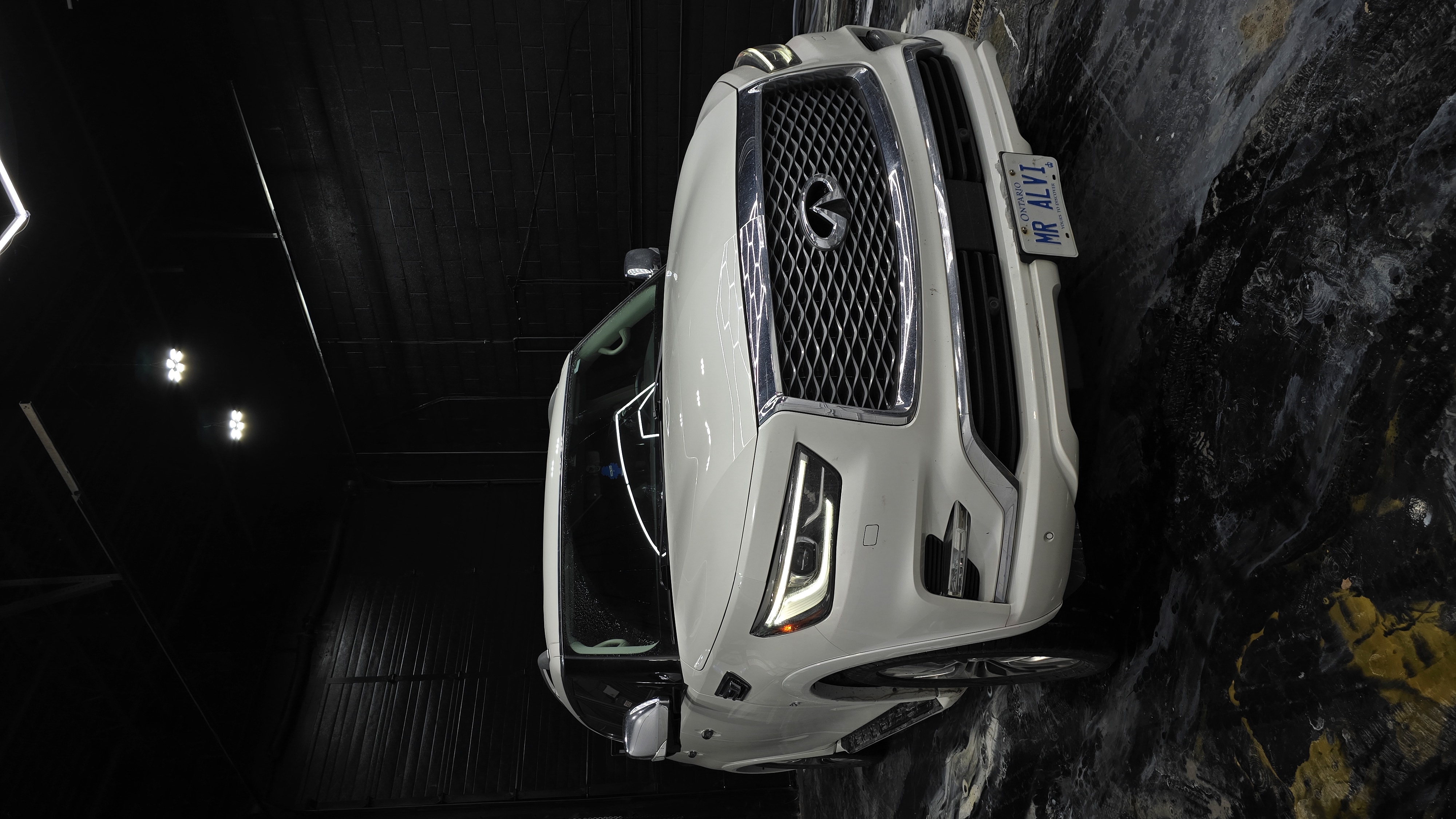 White Infiniti QX80 inside Jester Werks Mississauga studio after ceramic coating — gloss reflections under detailing studio lights